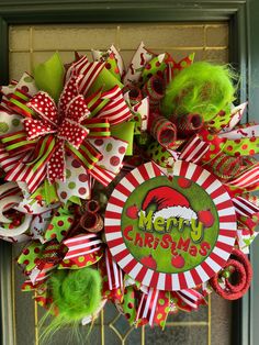 a merry christmas wreath with green and red bows on the front door, decorated with santa's helpers