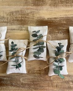 four napkins tied with twine and green leaves on top of each other, sitting on a wooden surface