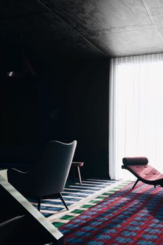 a living room with a chair, rug and large window in the background at night