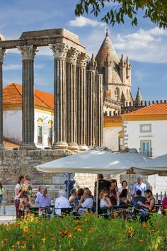 many people are sitting at tables in front of an old building with columns and arches