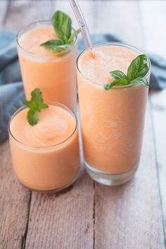 two glasses filled with orange juice and garnished with green leafy mints