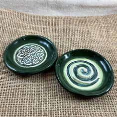 two green plates sitting on top of a burlock covered tablecloth next to each other