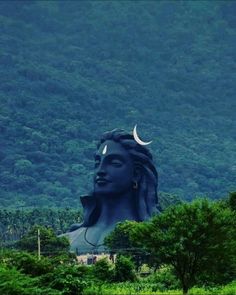 there is a large blue statue in the middle of trees and hills with a crescent moon on it