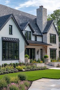 a large white house with black windows and lots of greenery in the front yard