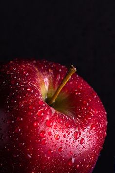 a red apple with water droplets on it's side and a glass next to it