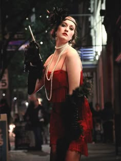 a woman in a red flap dress holding an umbrella and pearls on her head while walking down the street at night