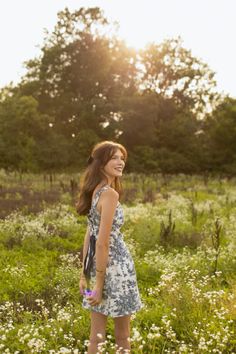 a woman is standing in the middle of a field with wildflowers and trees