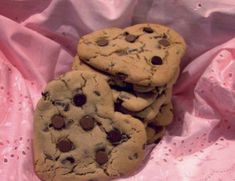 three chocolate chip cookies are stacked on top of each other in front of a pink background