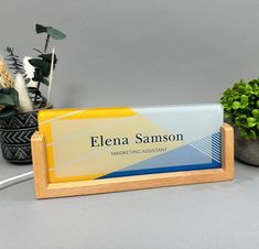 a wooden business card holder sitting on top of a desk next to potted plants