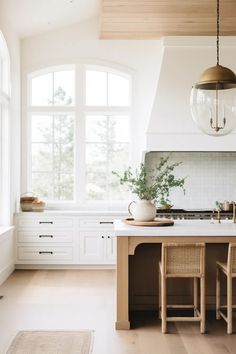 a kitchen with white cabinets and wooden flooring next to a large window that looks out onto the outdoors