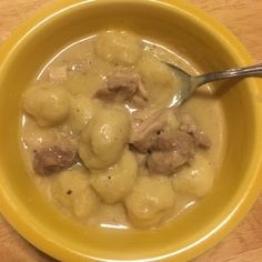 a yellow bowl filled with meat and dumplings on top of a wooden table next to a spoon