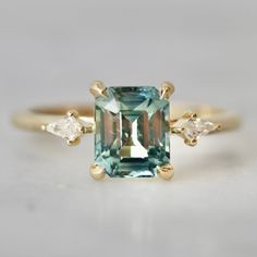 an emerald and diamond ring with three pear shaped diamonds on the band, set in yellow gold