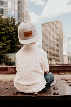 a young boy sitting on top of a wooden bench wearing a baseball cap and jeans