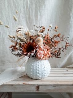 a white vase filled with flowers on top of a wooden table