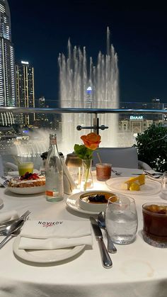 the table is set with food and water fountain in the background at night time,