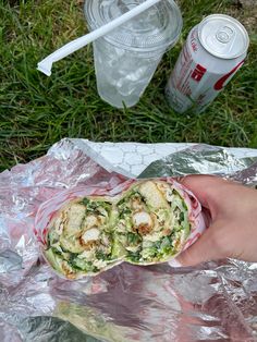 a person holding a sandwich in their hand on some tin foil with sodas nearby