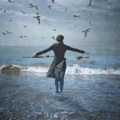 a woman is standing in the water with her arms spread out to seagulls