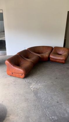 a brown leather couch sitting on top of a cement floor next to a white wall