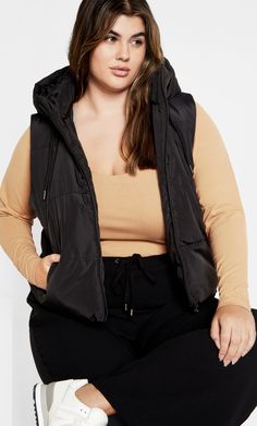 Enhance your winter style with the Ava Puffer Vest. The high neck hooded collar is both trendy and functional. Perfect for keeping warm from day to night, this vest is complete with a close fit a zip front opening. Key Features Include: - High neck hooded collar with draw-cord - Zip front opening - Sleeveless style - Close fit - Side zip pockets - Lined - Hip length hemline Layer with a knit jumper and cargo pants for an off-duty day look. | Plus Size Ava Puffer Vest in Black, Size 12 | City Chi Scoop Top, Plus Size Workwear, Explore City, Look Plus Size, Black Vest, Plus Size Top, Winter 2024, Cropped Denim, City Chic