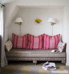 a couch with many pillows on top of it in front of a lamp and window