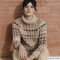 a woman sitting against a brick wall with her hands on her knees wearing a knitted sweater