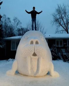 a man standing on top of a snow covered animal statue in front of a house