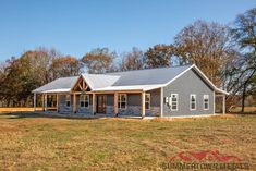 a large gray house sitting on top of a grass covered field in front of trees