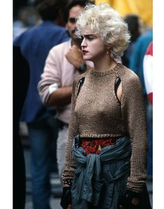 a woman with blonde hair wearing a brown sweater and green skirt standing on the street