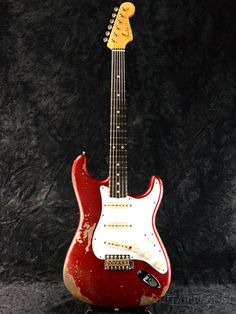 a red and white electric guitar sitting on top of a black background with its head turned to the side