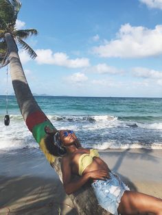 a woman laying on top of a palm tree next to the ocean