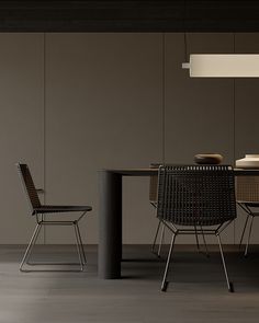 a dining room table with chairs and a lamp hanging from it's ceiling, in front of a gray wall