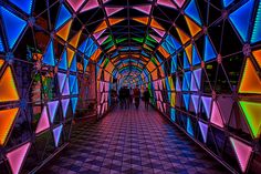 people are walking through a tunnel with colorful lights on the walls and floor, all in different colors