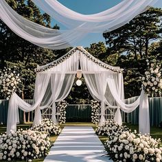 an outdoor wedding ceremony with white flowers and draping over the entrance to the aisle