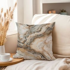 a marbled pillow on a couch next to a cup and plate with dried plants