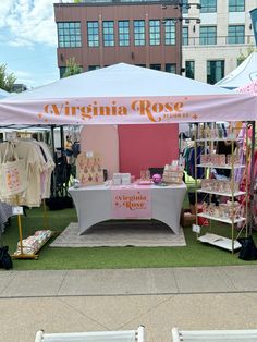 a tent set up with clothing on display in front of other tents at an outdoor market