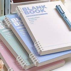 three notebooks are stacked on top of each other next to a pen and flower