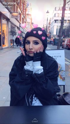 a woman sitting at a table with her hands to her face, wearing a black jacket and polka dot hat