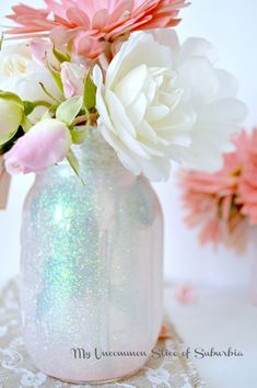 a white vase filled with pink and white flowers on top of a lace covered table