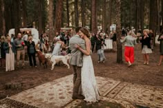 a bride and groom embrace in the woods surrounded by their guests at a wedding reception