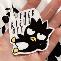 a hand holding a black and white sticker with the words f k right off on it