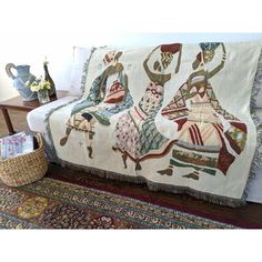 a couch covered in a colorfully patterned blanket on top of a wooden floor next to a basket