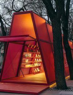 a red structure sitting next to a tree filled with lots of books on top of a wooden floor