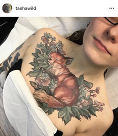 a woman laying on top of a bed covered in flowers and a fox tattoo next to her chest