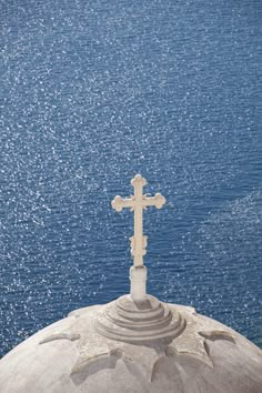 a cross on top of a building next to the ocean with blue water in the background