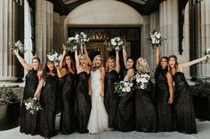 a group of women standing next to each other in front of a building holding bouquets