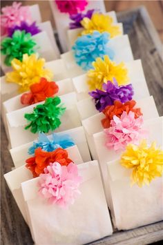 small bags with colorful flowers on them are sitting on a wooden table, ready to be used as place cards