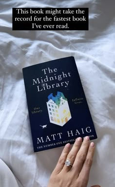 a person's hand on top of a book with the title, the midnight library