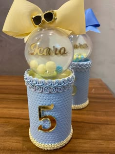 two snow globes sitting on top of a wooden table with a yellow bow around the top