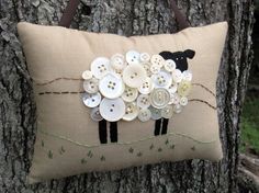 a pillow with buttons on it is sitting next to a tree trunk and has a sheep design on the front