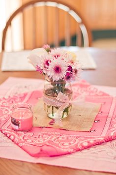 pink flowers are in a glass jar on a table with a napkin and candle next to it